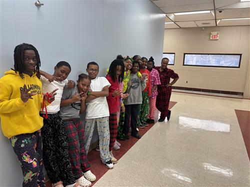 11 students posed in front of a blue wall with different facial expressions wearing pajamas along with an adult.