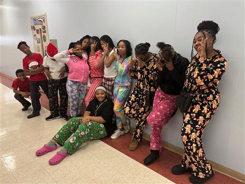 12 students in a hallway in front of a blue wall wearing pajamas, posing for a picture. 