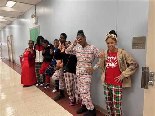 7 students posed in pajamas in a hallway with an adult, wearing different facial expressions.