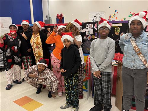 8 students wearing pajamas inside of a classroom posed with an adult.