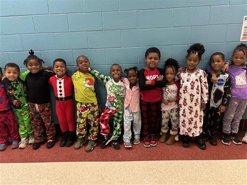 11 students posed in front of a blue wall with different facial expressions wearing pajamas. 