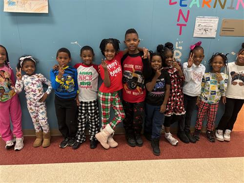 11 students posed in front of a blue wall with different facial expressions wearing pajamas. 