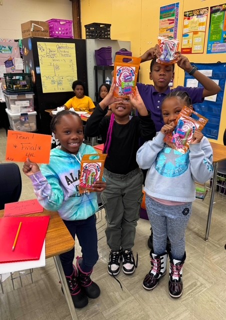 four students holding up prizes and smiling