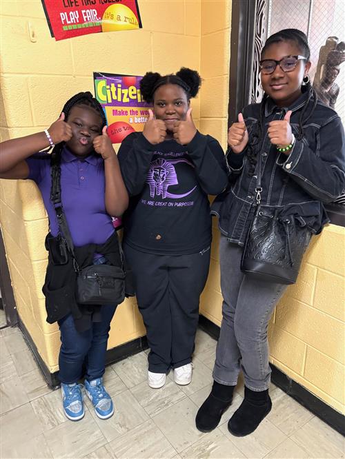 three girls standing, smiling and giving thumbs up