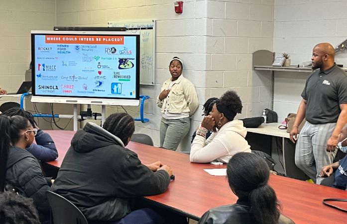  a person standing by a board and talking to students