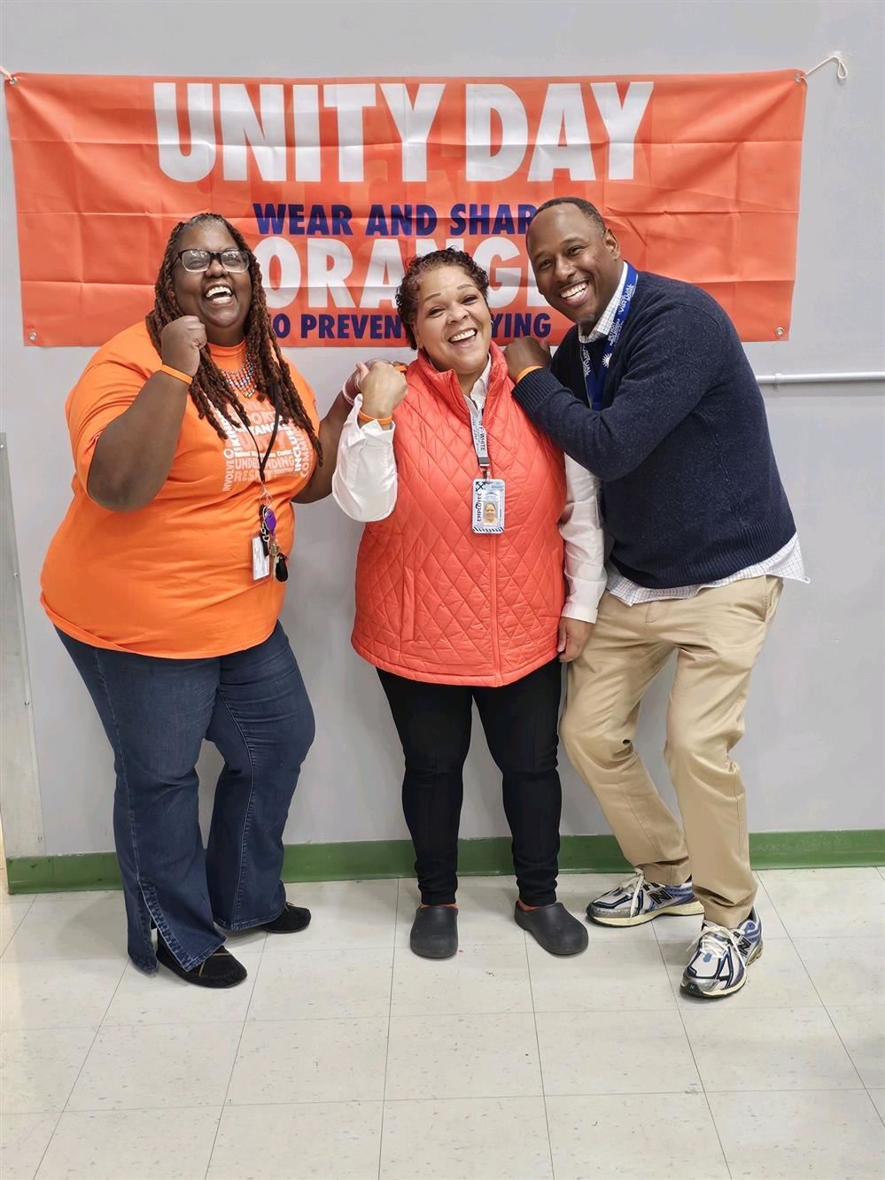 three school staff members smiling in front of unity day banner