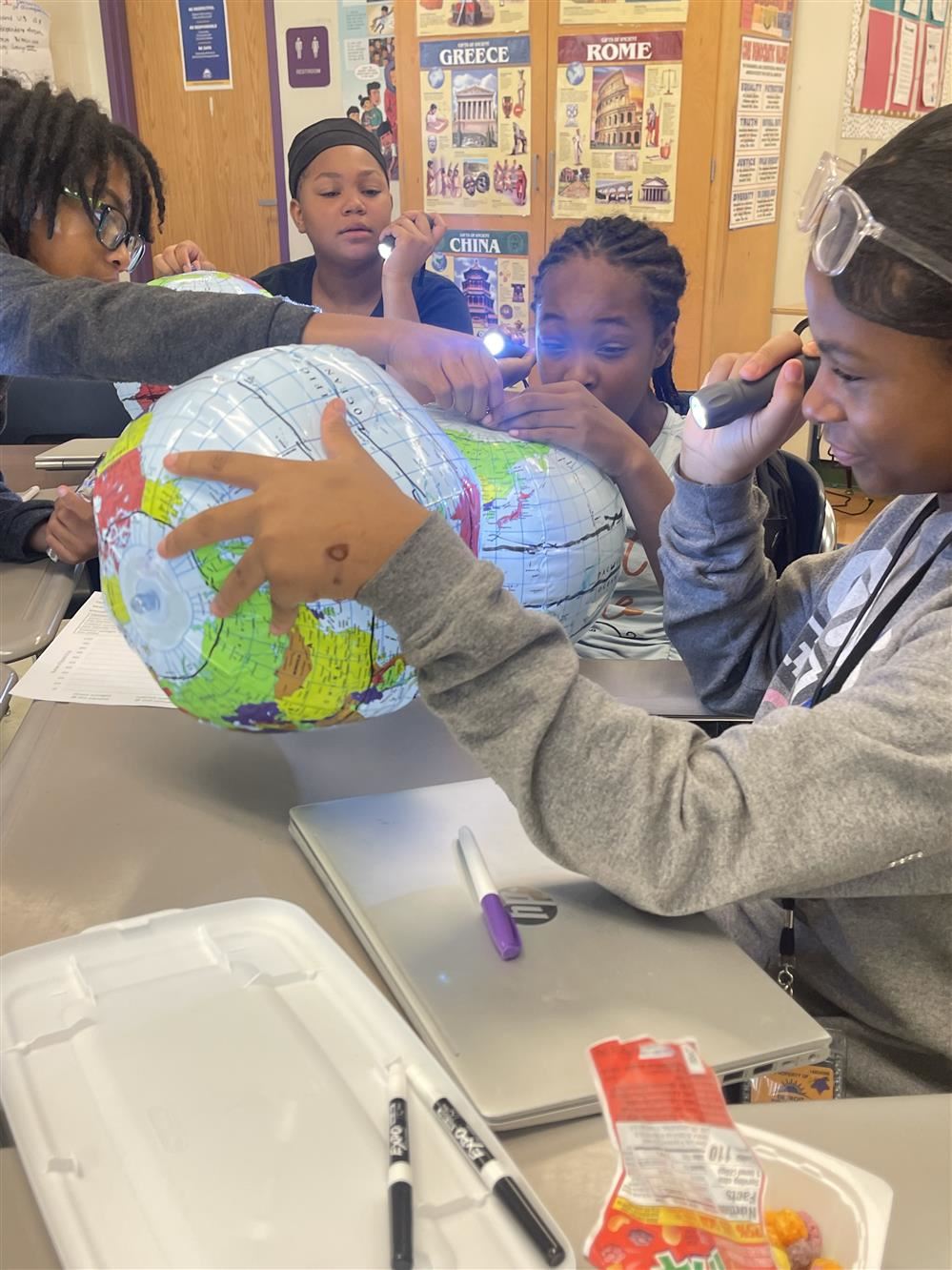  students looks at a globe with flashlights