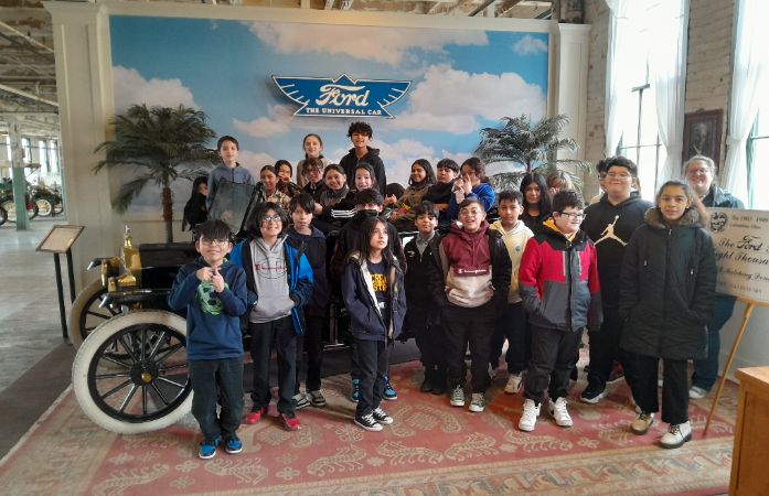  students sitting and and standing around a vintage car