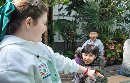  students with a butterfly on her hand as two students look on