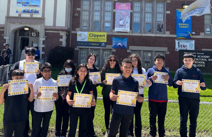  student standing outside of school building with certificates