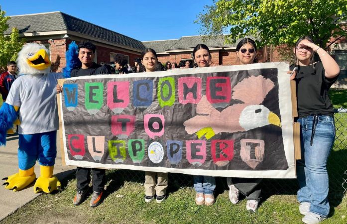  students standing with a welcome to Clippert banner in front of the school building