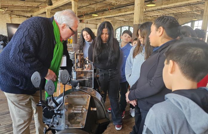  students listening to docent showing how a motor works