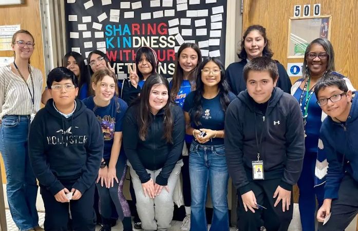  students and staff standing in front of veteran's poster