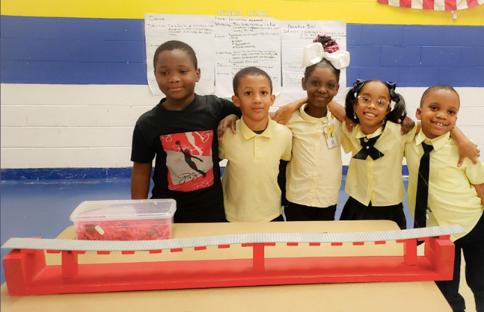  5 students standing behind their lego bridge with arms around each other