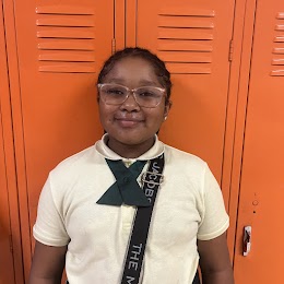 5th grade student smiling at camera in front of orange lockers