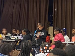 student on stage giving reading speech with a microphone to a group of students