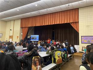 image of cafeteria and student standing on stage giving a speech while all students listen