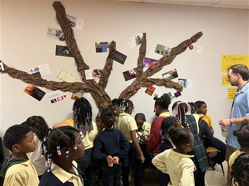 group of students in hallway listening to 4th grade students read poems in front of poem tree