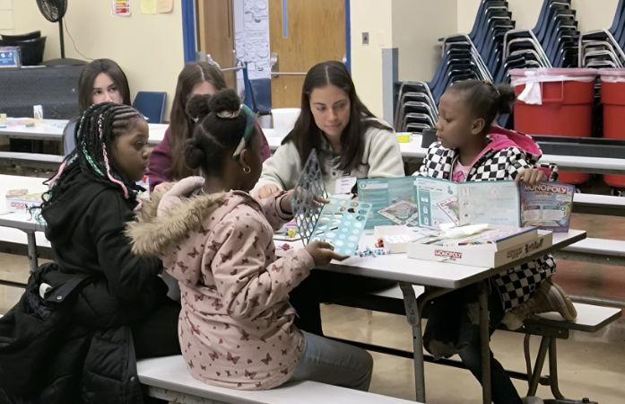 3 elementary school students and 3 high school students sitting at a table playing monopoly