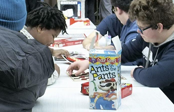 two students playing checkers at a table with other board games on it