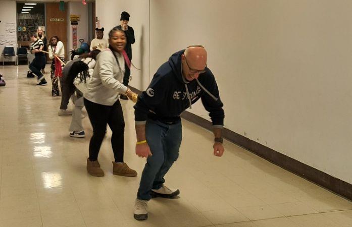 group of students and adults playing tug of war in school hallway