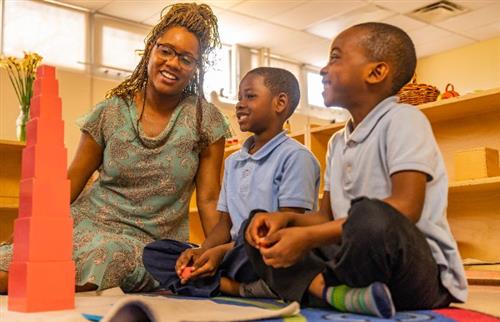 teacher and 2 students sitting on rug with blocks