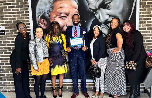  Man holding an award with 6 women standing around him.