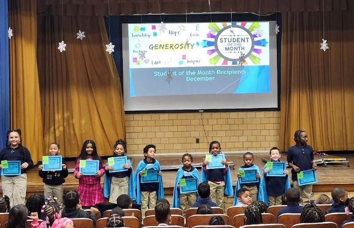  10 children standing in front of a stage hold up their award.   