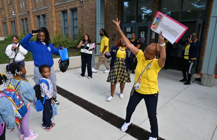  students walking into school, teacher holding a sign.