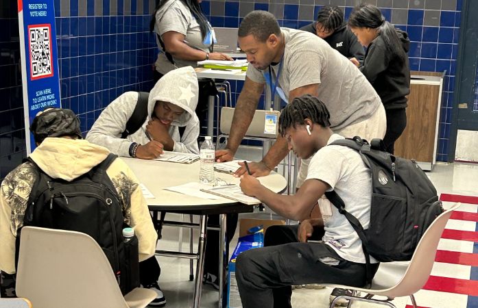  students sitting at lunch table filling out a voter registration application