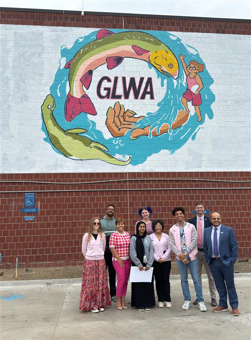  Students and educators standing in front of a brick wall with an almost finished fish themed mural.