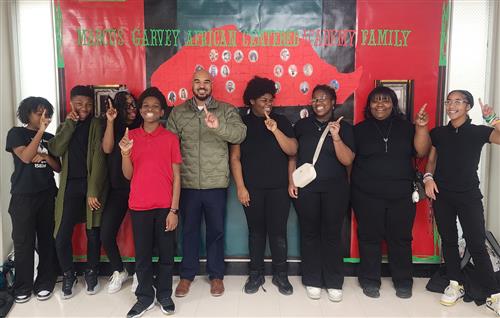 Students and male teacher smiling with index finger up in the air
