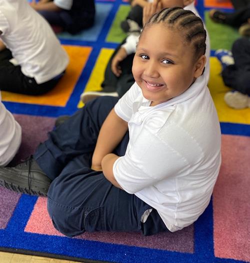 A student smiling sitting down on the carpet.
