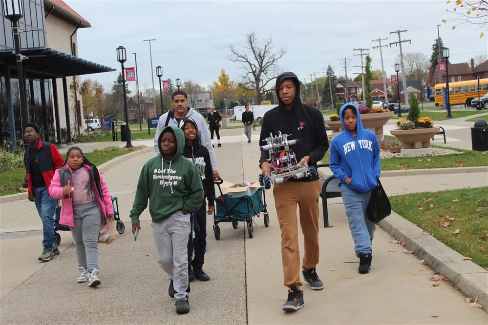 Robotics students walk with robot toward camaera.