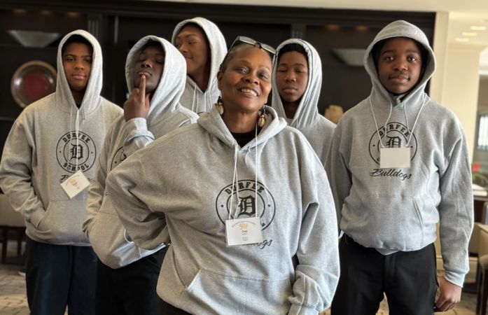 A female is standing with boys with hoodies.