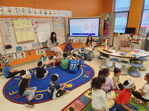  Two high school girls reading to kids sitting on a colorful carpet 