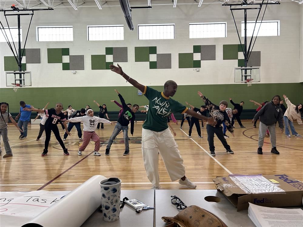  woman dancing in a gymnasium with students watching 