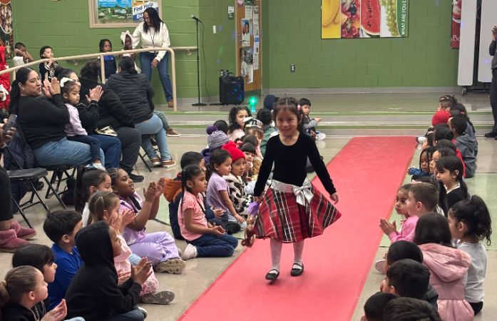  girl walking down a runway with adults and kids clapping