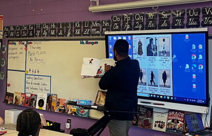  man holding a book standing up in a classroom 