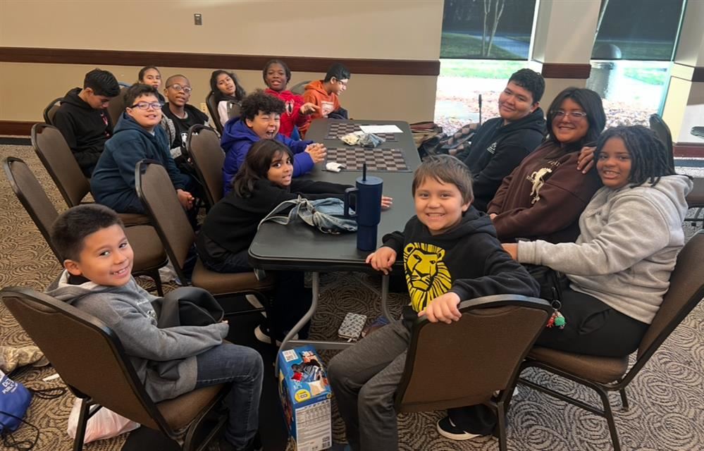  students sitting at a table smiling with a chess board