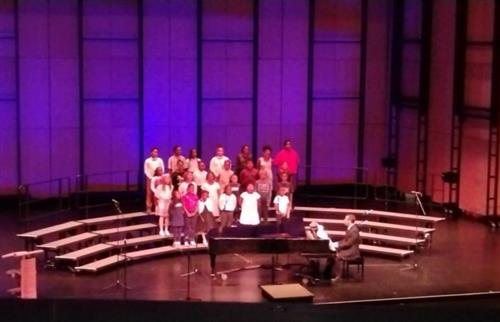 students on stage singing accompanied by a piano