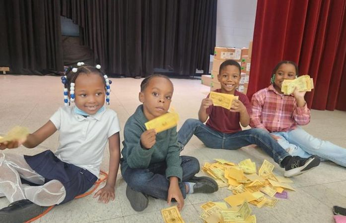 students sitting on stage with their FLICS bucks