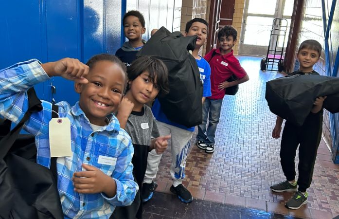  students smiling holding bags in hallway