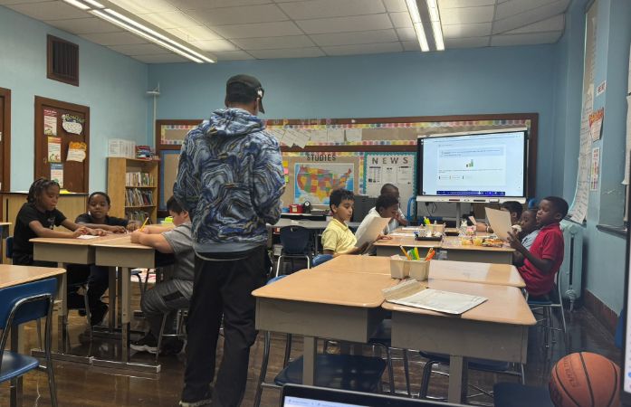  male standing with students sitting at a desk 