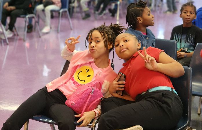  Two students sitting next to each other holding up peace fingers