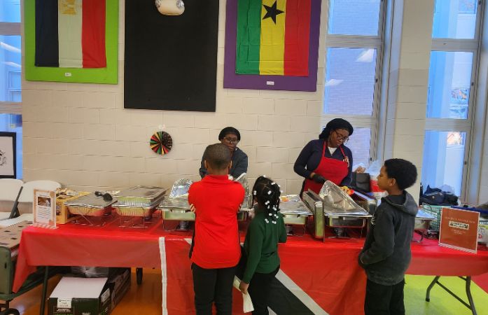  Three young students waiting in line to be served food from two women
