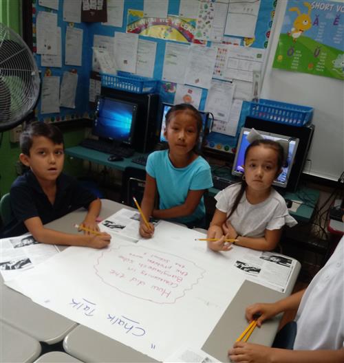 three 2nd grade students writing responses on chart paper 