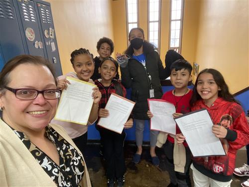 Principal Ramos taking a selfie with the 5th graders proudly holding their written work and showing it off