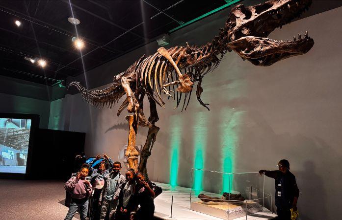  students posing for picture in front of T Rex skeleton model